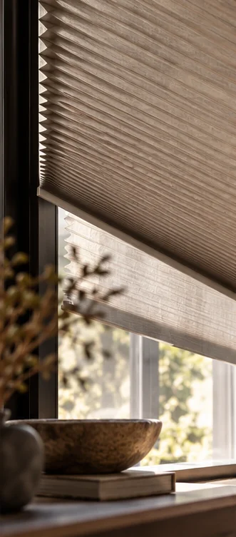 Plissé gordijn voor een raam met een houten schaal en droogbloemen op de vensterbank