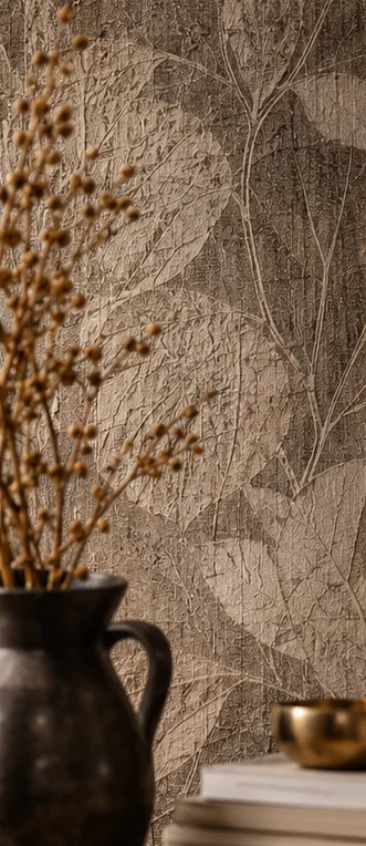 Behang met een reliëf van bladeren achter een donkere kan met droogbloemen