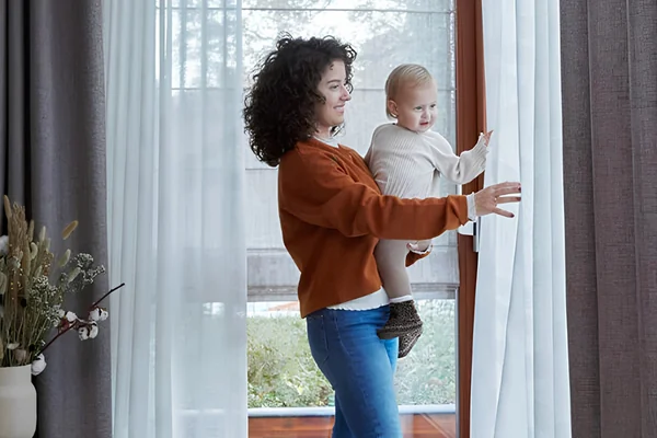 Witte vitrage Vadain met grijze overgordijnen - AC Mooi Wonen Culemborg Vrouw met kind bij witte vitrage Vadain en grijze overgordijnen voor een tuindeur